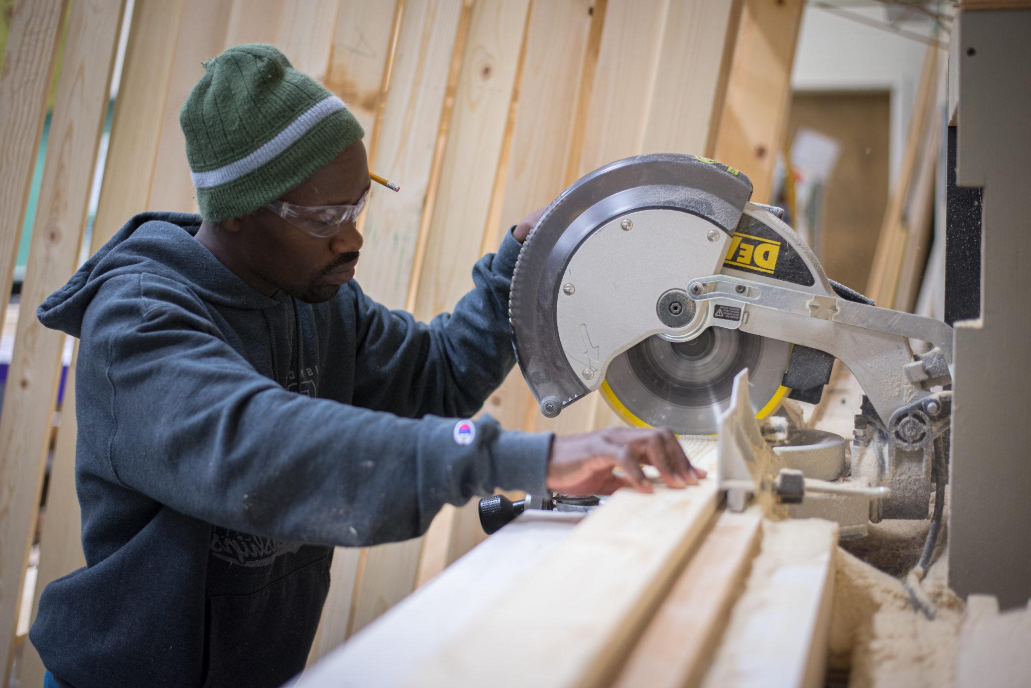 Student operating a vertical circular saw on a plank of wood