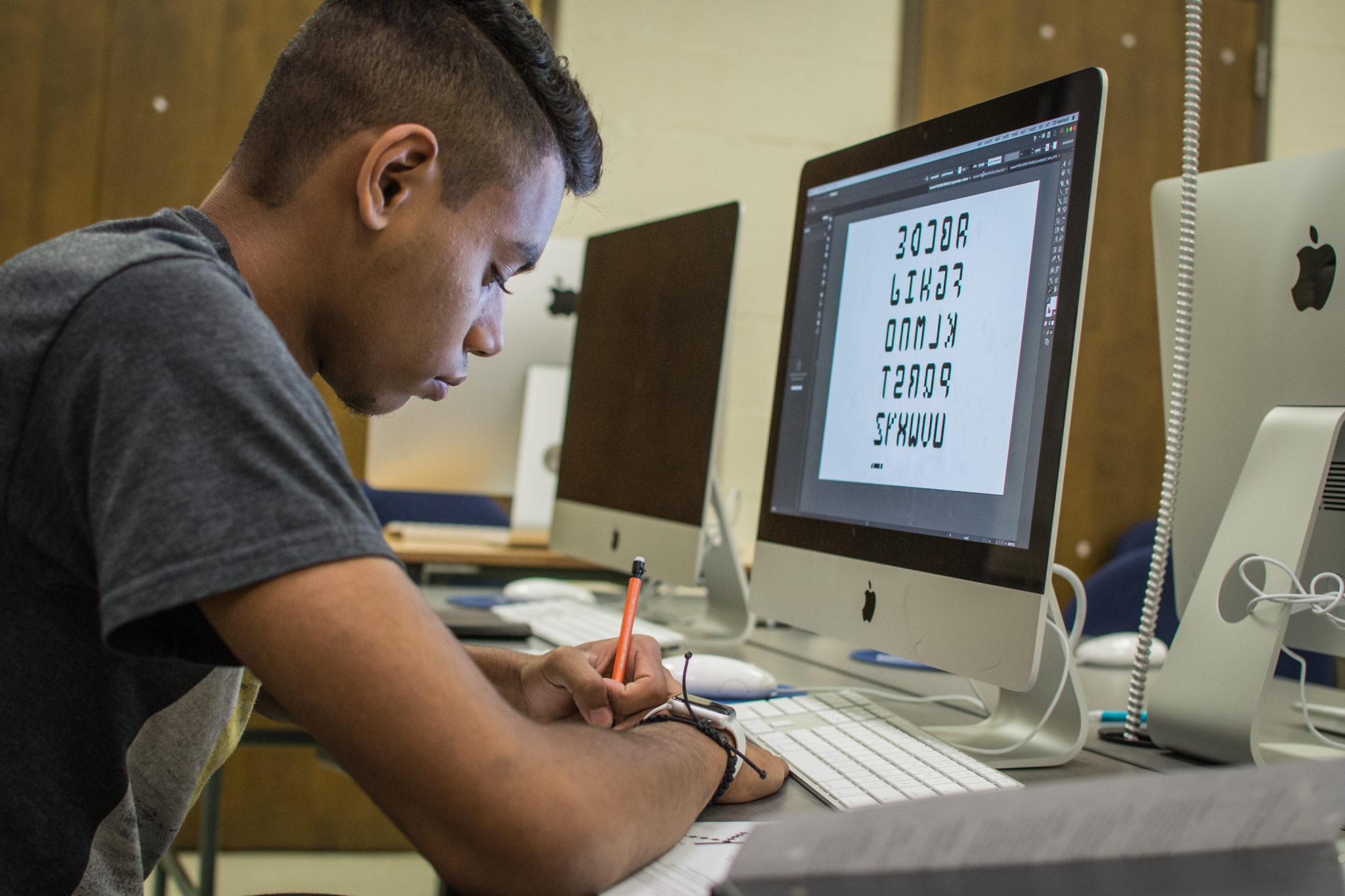 Student writing at a desk with a computer